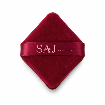 A deep red velvet makeup sponge with a satin ribbon band featuring the brand name 'SAJ BEAUTIE' in white, set against a plain white background.